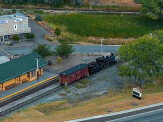 Aerial image of a train station in Carson City, Nevada, with a vintage locomotive, green roofed depot, Comstock History Center, and surrounding greenery.