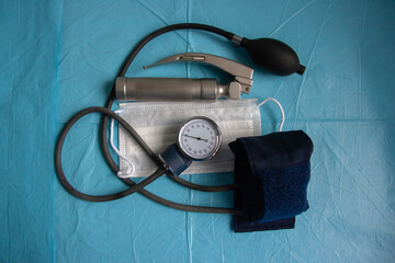 On the table are a laryngoscope, a tonometer, and a medical mask. On a blue background.