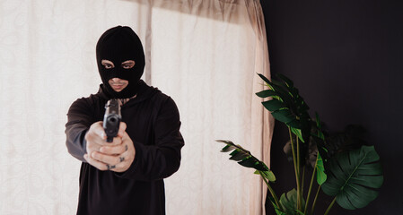 A hooded robber with a gun breaks into a house.