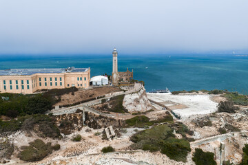 Alcatraz Island in San Francisco Bay features the iconic prison complex, a central lighthouse, rocky terrain, sparse vegetation, and blue waters.