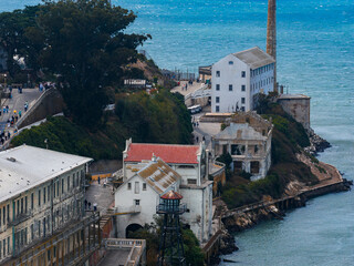 View of Alcatraz Island in San Francisco Bay, featuring the white prison building, lighthouse, red roofed structure, rugged coastline, and visitors.