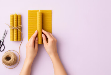A woman's hands make beeswax candles against a soft lavender, pastel background.
