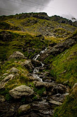 Moody Alpine Stream Cascading Over Dark Rocks on a Steep Slope under Gray Sky