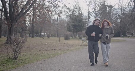 A young couple enjoys a leisurely stroll through a park, sipping coffee and sharing laughter on a serene day. - Powered by Adobe