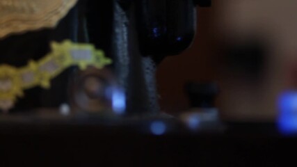 Macro shot of a sewing machine needle rapidly stitching red fabric. Bokeh effect of colorful Christmas lights twinkles in the dark background, ideal for holiday crafting themes.