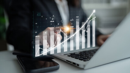 A business professional reviews financial data on a laptop, highlighting growth through virtual graphs and modern analytics in a professional office setting. Impute