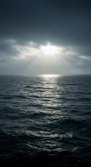 Fototapeta premium Sun breaking through stormy clouds over a dark ocean. Dramatic weather concept. Natural background or abstract texture for design.