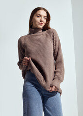 A beautiful woman in a beige knitted sweater poses on a gray background