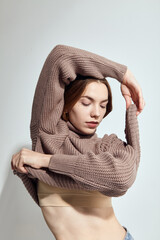 A beautiful woman in a beige knitted sweater poses on a gray background