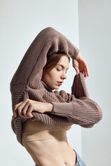 A beautiful woman in a beige knitted sweater poses on a gray background
