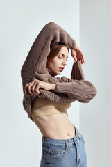 A beautiful woman in a beige knitted sweater poses on a gray background