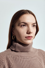 A beautiful woman in a beige knitted sweater poses on a gray background