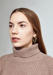 A beautiful woman in a beige knitted sweater poses on a gray background