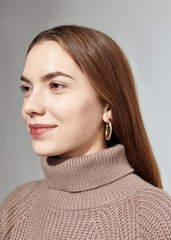 A beautiful woman in a beige knitted sweater poses on a gray background
