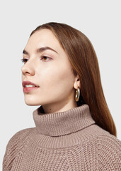 A beautiful woman in a beige knitted sweater poses on a gray background