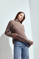 A beautiful woman in a beige knitted sweater poses on a gray background