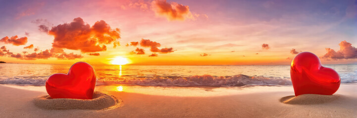 Stunning orange sunset on a calm beach with two plush red hearts