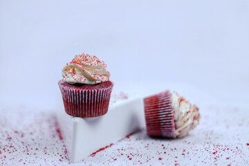 A close-up of red velvet cupcakes topped with creamy frosting and red sprinkles, displayed on a white surface, creating a minimal yet elegant dessert presentation.