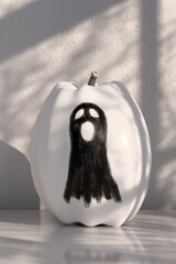 Black and white pumpkin decorated with silhouette of ghost on kitchen table. Pumpkin painted in monochrome colors, decorated decoupage technique. Home decoration for Halloween