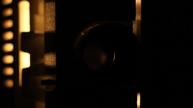Close-up view of a blindingly bright cinema projector lens emitting intense white light. The beam dims and switches off, transitioning to complete darkness.