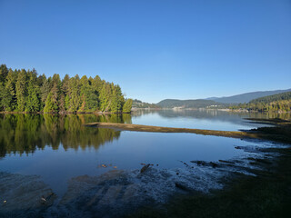 Tranquil Lake Scene With Forested Shoreline And Snow-Free Mountains In Port Moody, British Columbia, Canada