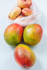 Contemporary still life showing ready-to-eat mangoes and peaches at their peak inside plastic bags on a wooden surface