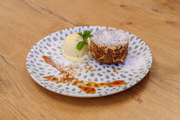 Chocolate lava cake with vanilla ice cream, crushed nuts and powdered sugar, artistically plated on dotted ceramic plate on wooden table in cozy restaurant.