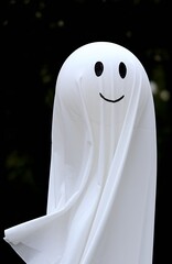 A friendly ghost decoration crafted from a white sheet and balloon, gently swaying in the wind with a simple, happy drawn face.
