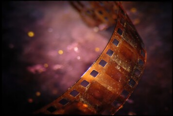 A curled strip of aged film, golden-brown hue, with a soft bokeh effect in the background