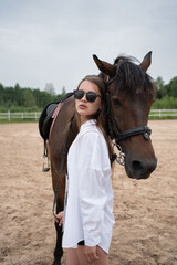 A serene woman standing with a brown horse near a stable. Hippotherapy. The year of the horse