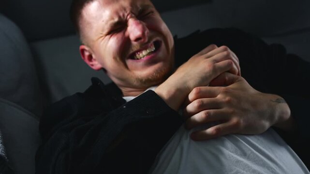 A young man suddenly suffers a heart attack while lying on a gray sofa in a room.
A man suffers from heart pain.
A man clutches his heart during a heart attack.