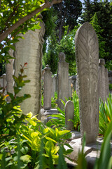 Naklejka premium Old stone gravestones with intricate carvings surrounded by greenery in a peaceful cemetery. Concept for history, remembrance, and cultural heritage.