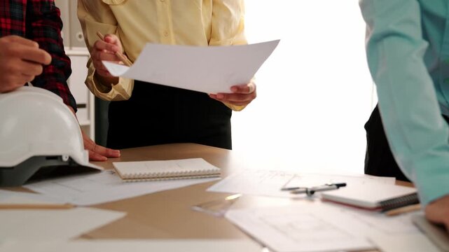 Architect and safety engineer discussion about building blueprint displaying on laptop on table with architectural document and wooden block scatter around at modern office. Closeup. Delineation.