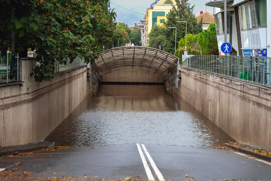 Fototapeta Flooded underpass blocks city road, with fallen leaves and rain-soaked asphalt in the foreground. Concept of flooding, stormwater, and dangerous road conditions