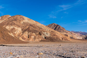 Warm-Toned Sunlit Desert Hills Rising Beyond Rocky Foreground Under Bold Blue Sky