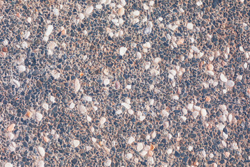 Textured surface exposed aggregate concrete, characterized by numerous small, irregular stones embedded within binder. Varied shades of pebbles create detailed naturalistic pattern across entire frame