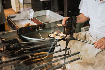 Close-up of a vendor cooking Japanese sweets in a metal mold at a Tokyo street stall. Concept for authentic cuisine, tradition, and local street culture.