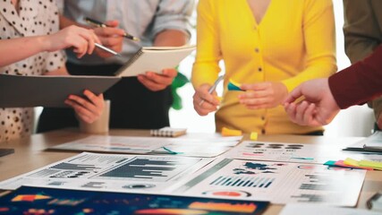 A diverse team engages in a collaborative meeting, analyzing data charts and discussing strategies with digital tools and documents spread across a modern office table. SACTR - Powered by Adobe
