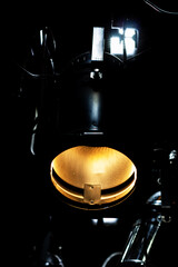 A striking close-up of a warm, golden stage spotlight isolated in profound darkness. The intense light source creates a powerful, dramatic glow with sharp contrasts.

