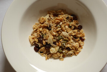 Granola mix showing oats, nuts, seeds, and dried fruit in a white bowl. Cotswolds countryside, England