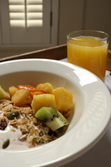 Bowl of fresh fruit, granola, and yogurt with a glass of orange juice on a wooden tray. Cotswolds countryside, England