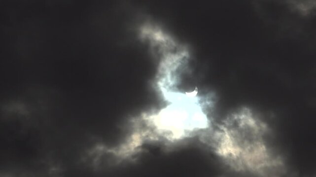 Soft light slices through gray clouds, showing a vivid partial solar eclipse seen through an overcast sky.