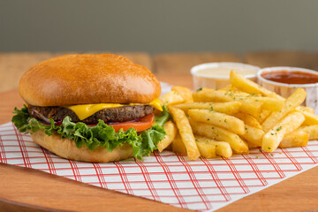 Cheeseburger with fries and sauces on wooden table