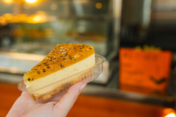 Hand holding a passion fruit cheesecake slice inside bakery