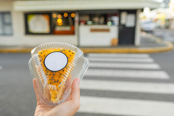Hand holding a slice of passion fruit cake in front of a street cafe