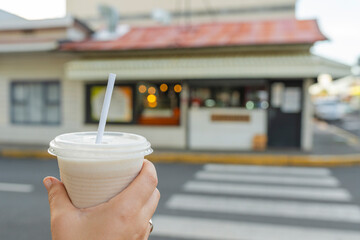 Hand holding a smoothie cup in front of a street cafe