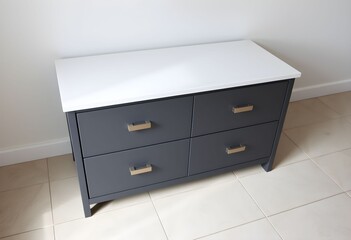 A modern dark gray four-drawer dresser with a white top and metallic handles, standing on a tiled floor against a white wall.