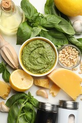 Fresh pesto sauce in bowl, ingredients and squeezer on white table, flat lay