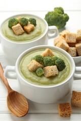 Tasty broccoli cream soup with croutons served on white wooden table, closeup