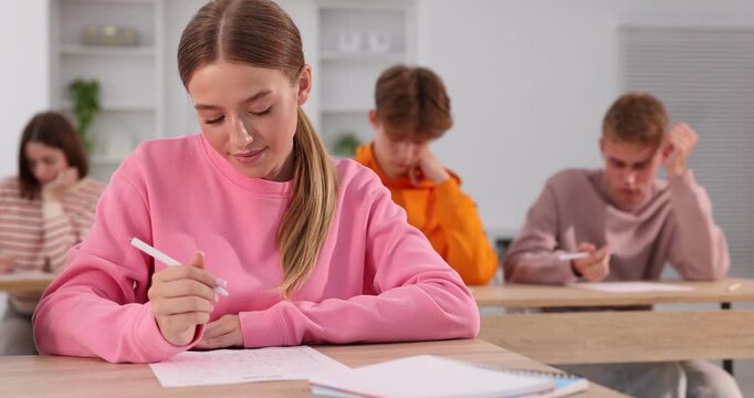 Students taking exam at wooden table indoors, selective focus